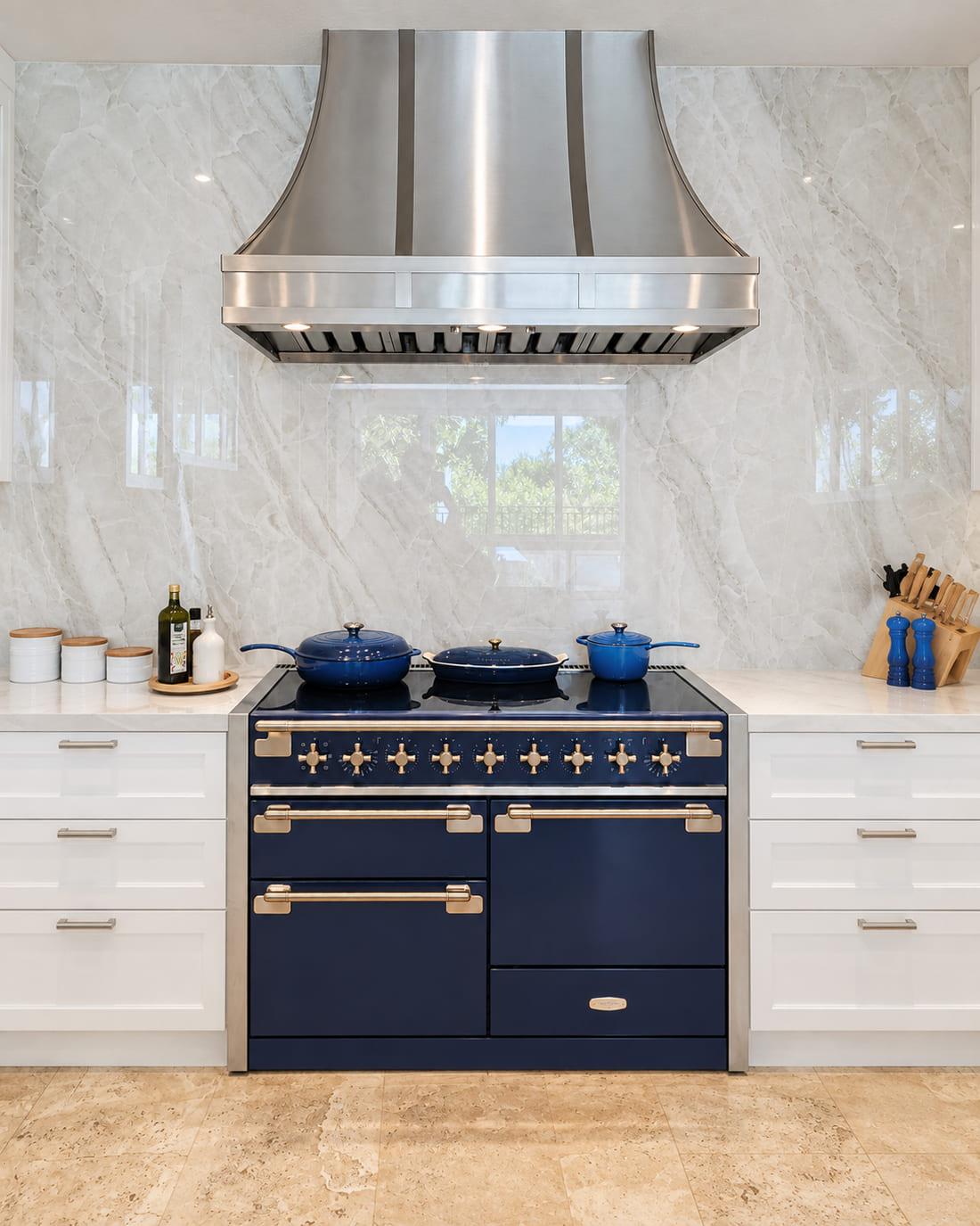 Cobalt range with brass trim under a stainless hood, against a book-matched marble wall