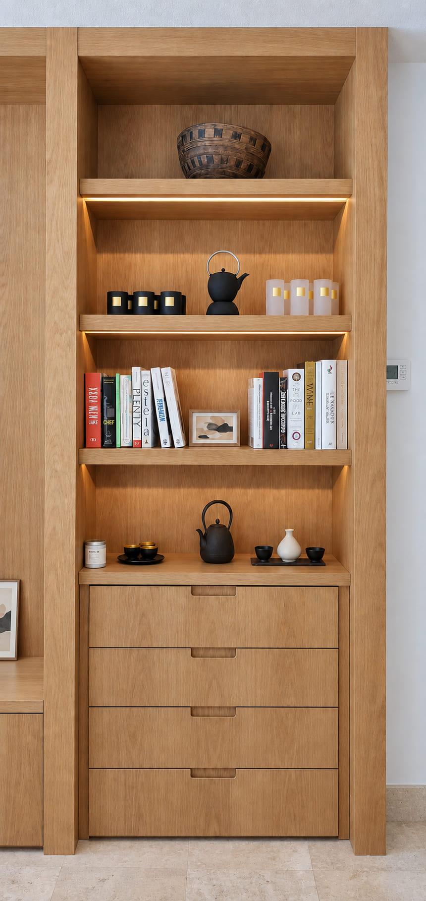 A bay of the oak library with lit shelves above four brass-pulled drawers