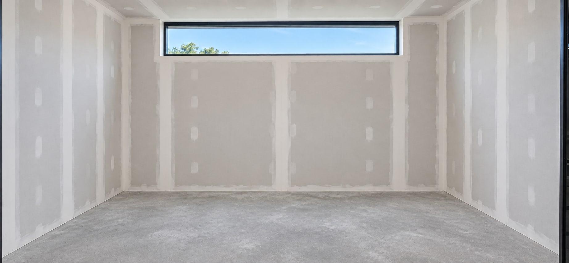 The dressing room as received: taped drywall, a concrete floor and a clerestory window in the back wall
