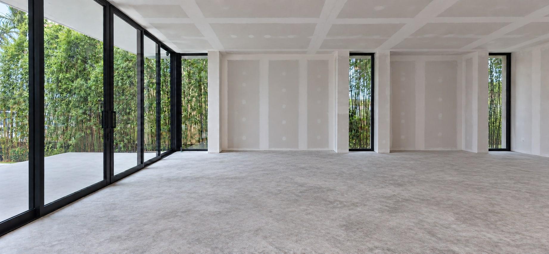 The living room as received: taped drywall, a bare concrete floor and sliding glass onto bamboo