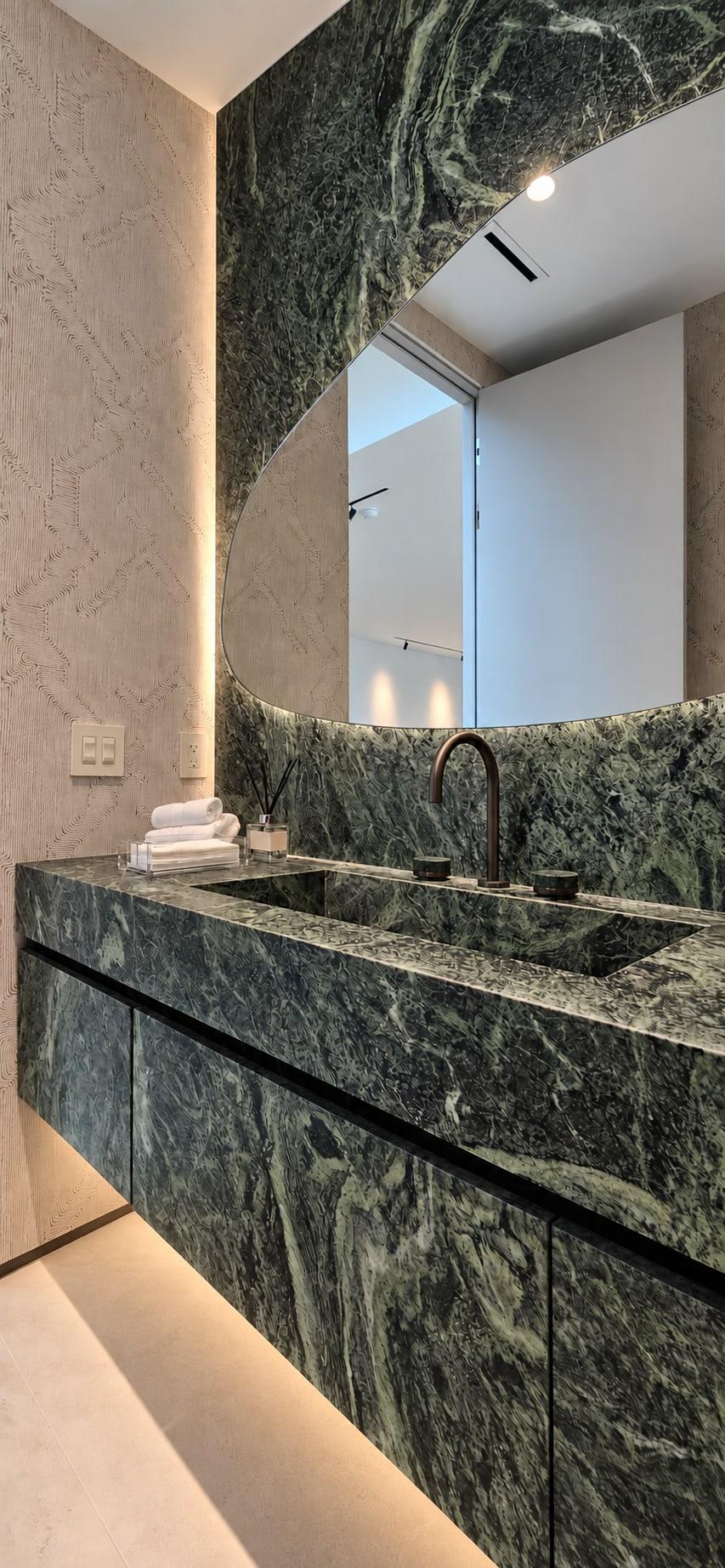 Floating green marble vanity with an integrated basin, under a mirror cut into a green marble wall