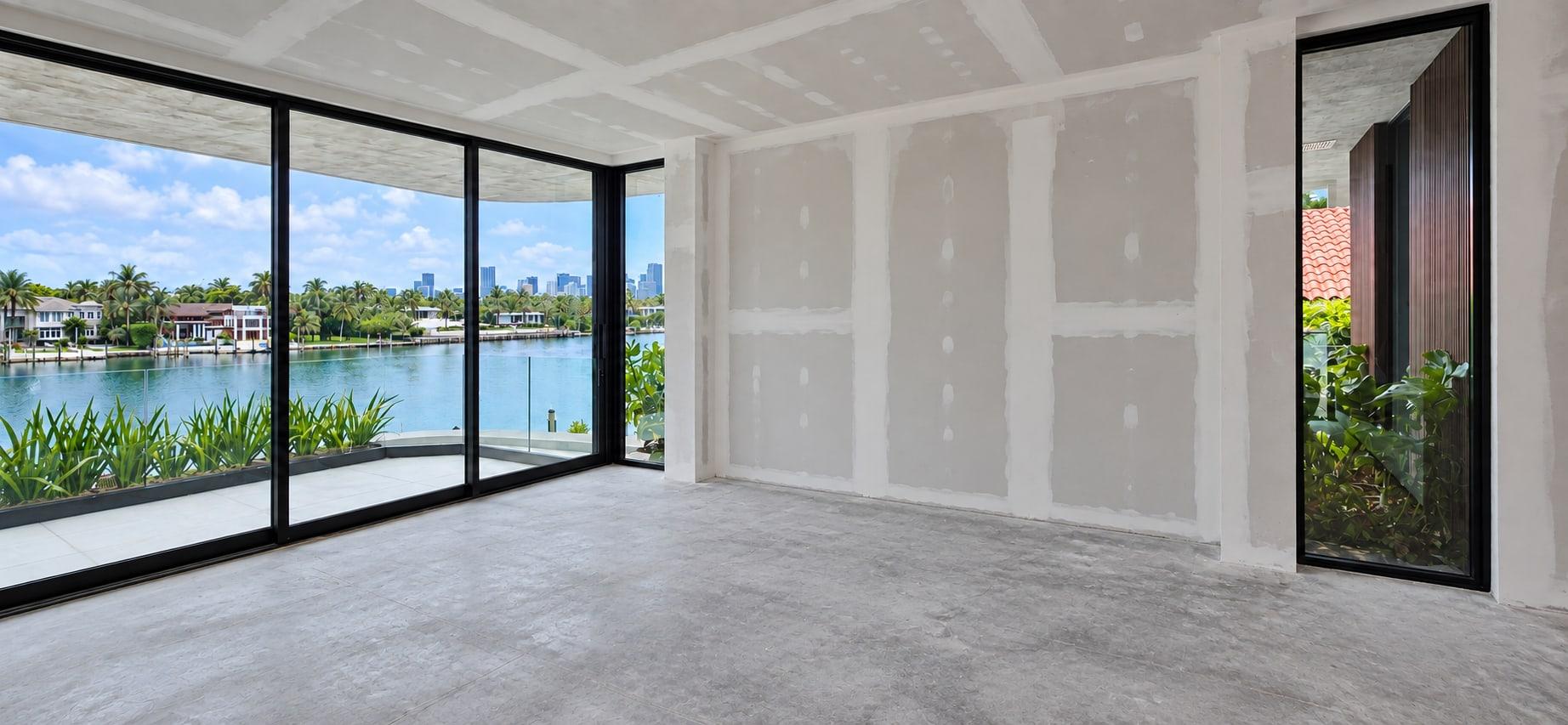 The primary suite as received: taped drywall, a concrete floor and glazing onto the bay and the skyline