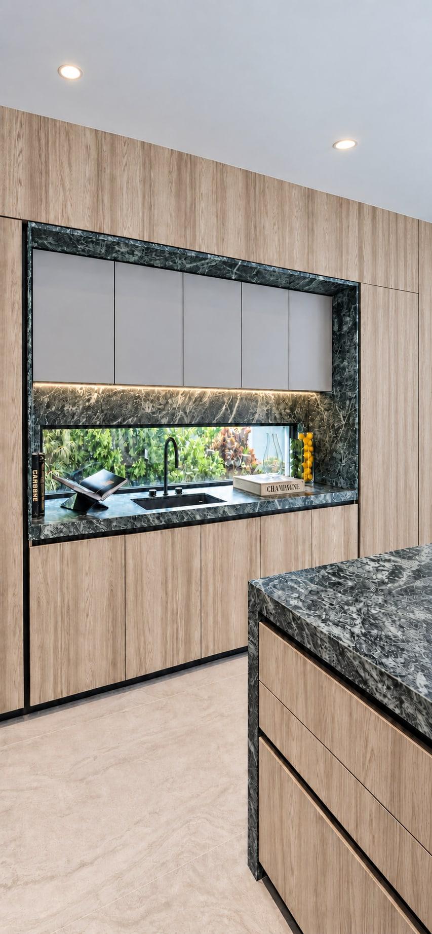 Kitchen window splashback framed in green marble under pale flat-fronted wall units, inside a full-height oak run