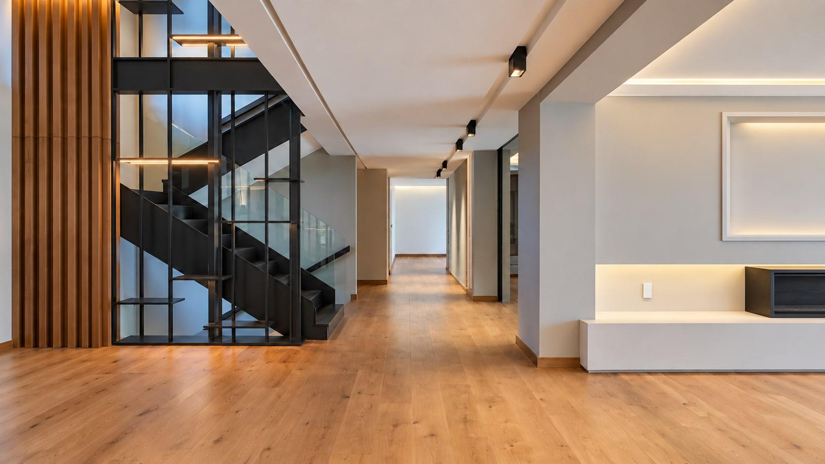 Long oak-floored corridor with the steel and walnut stair screen on the left and a lit fireplace niche on the right
