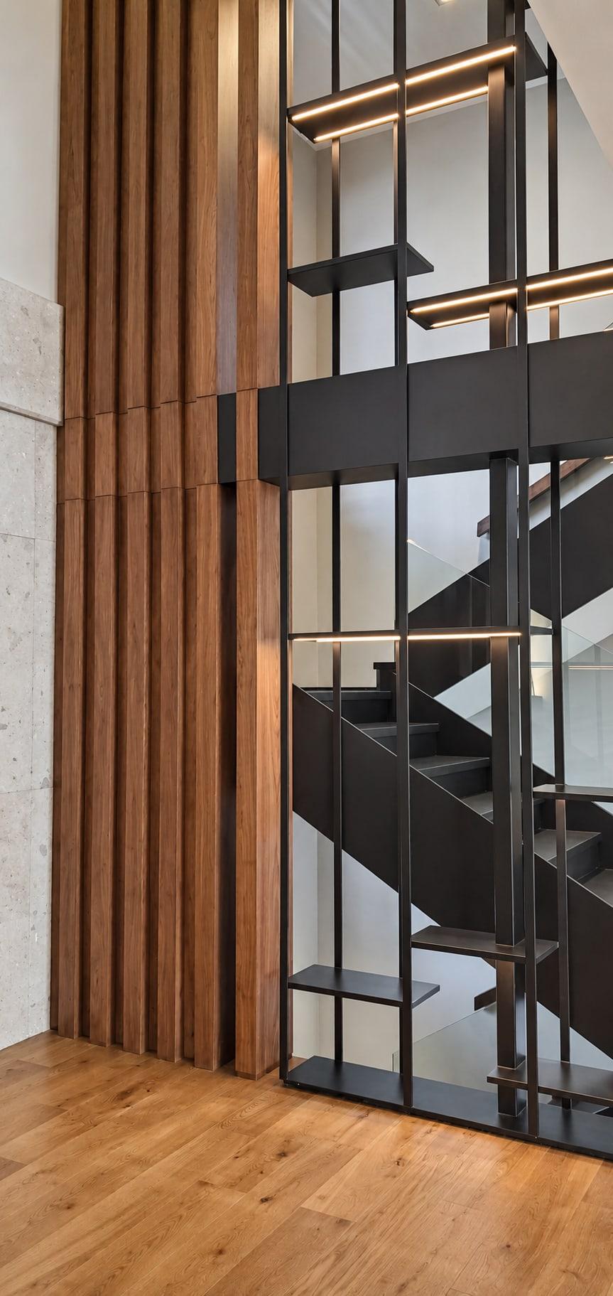 Full-height walnut fins beside a blackened steel stair screen with lit shelves