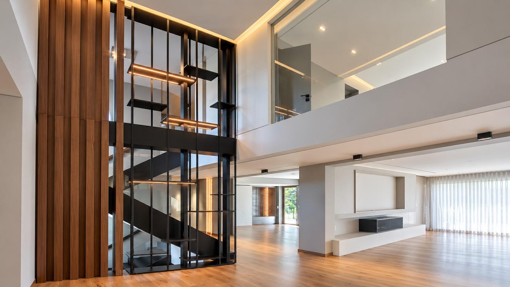 Walnut fins and a blackened steel stair screen with lit shelves rising through a double-height hall