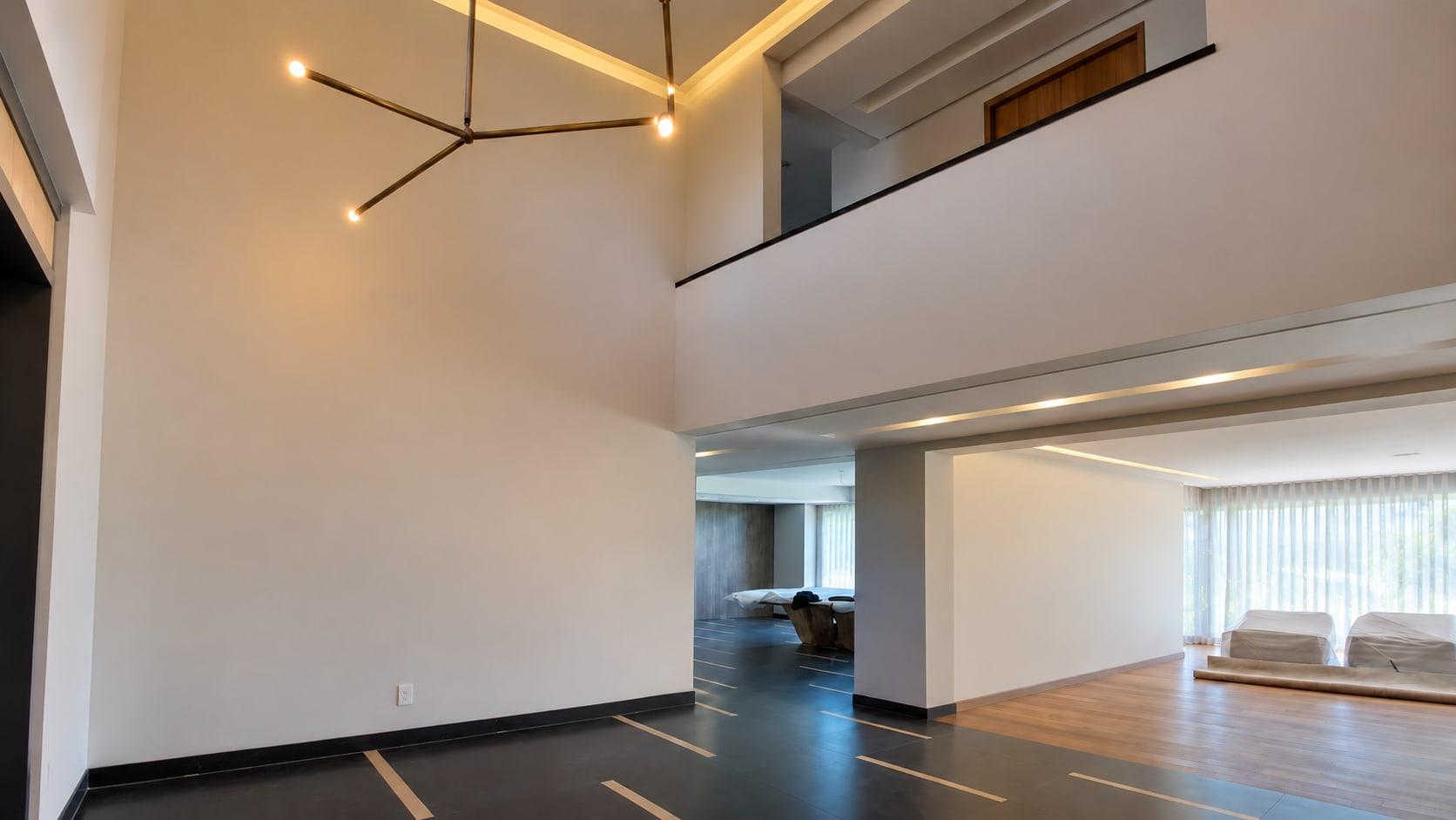 The double-height hall as received: a white wall two storeys high, a branching chandelier and a dark tiled floor