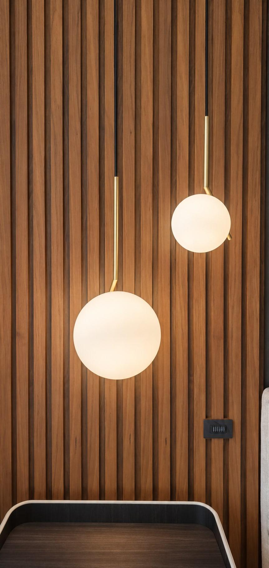 Two opal glass globe pendants on brass rods hanging against walnut slats over a bedside table