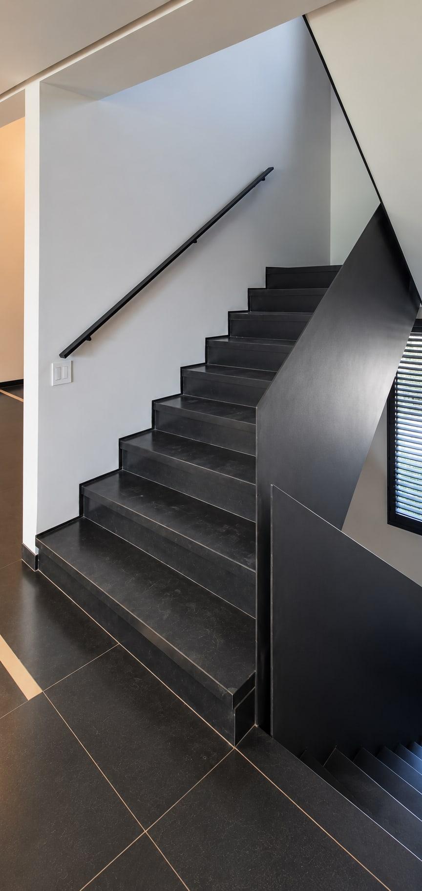 The stair as received: black tiled treads, a black handrail on a white wall and a solid black balustrade