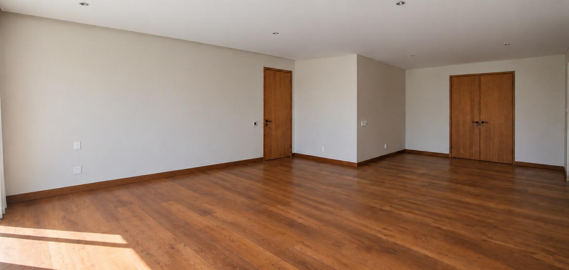 The primary suite as received: plain walls, a dark wood floor, a single door and a pair of double doors