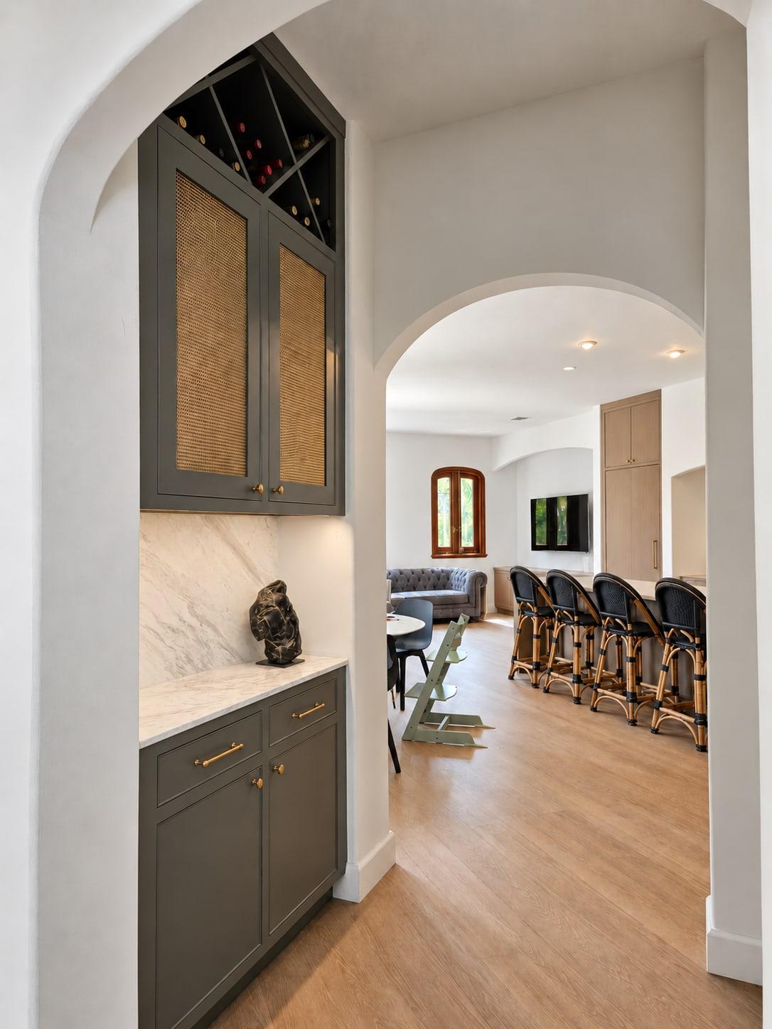The green bar cabinet seen through an arch, with the kitchen island and the living room through a second arch beyond