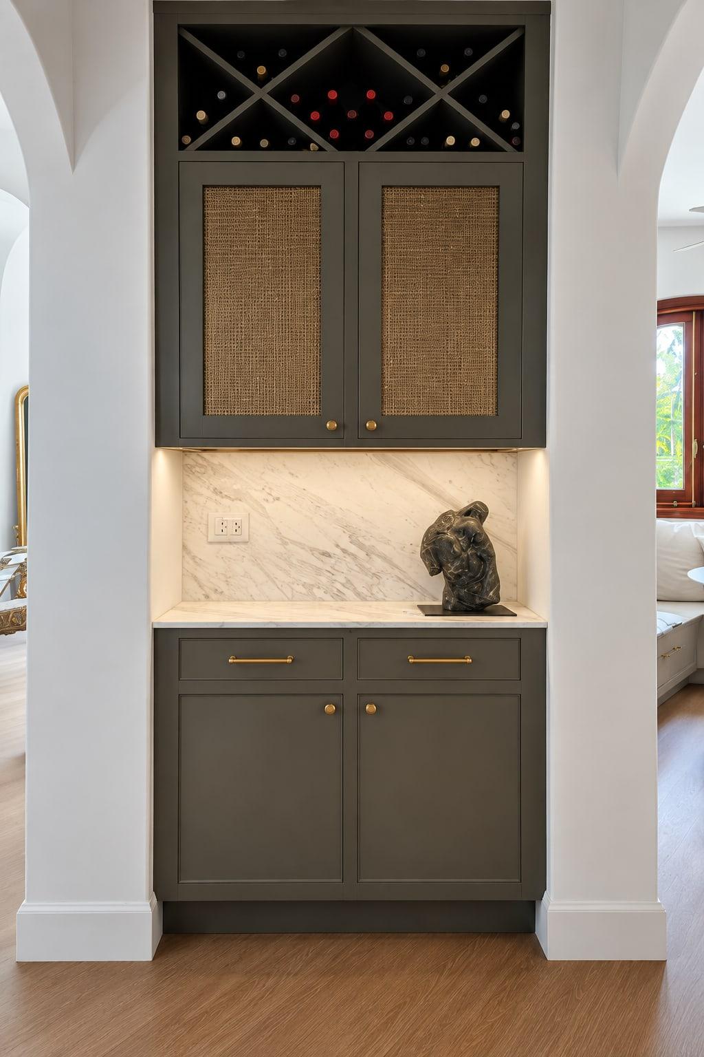 Bar cabinet in grey-green lacquer between two arches: wine in a diagonal rack, cane-panelled doors, a lit marble back and cupboards below