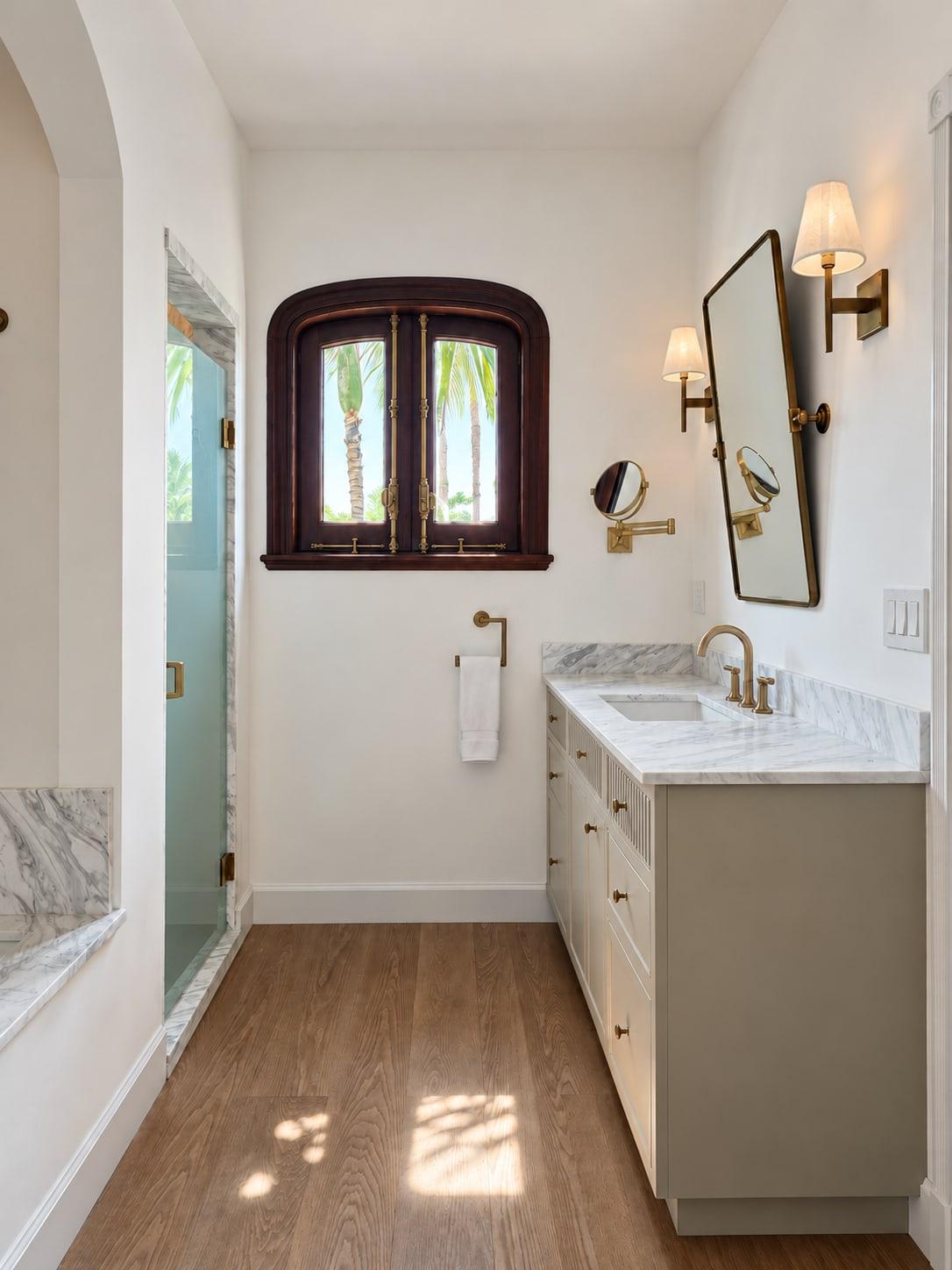 Bathroom with a long painted vanity and marble top beside an arched mahogany window, with a glass shower door on the left