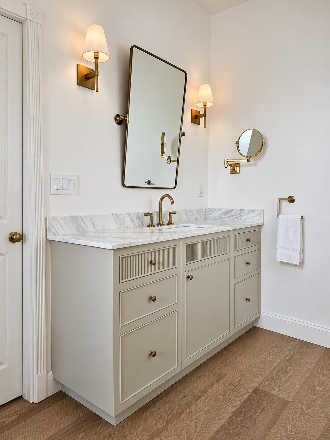 Pale sage painted vanity with reeded drawer fronts, a white marble top, a brass tap and brass wall lights