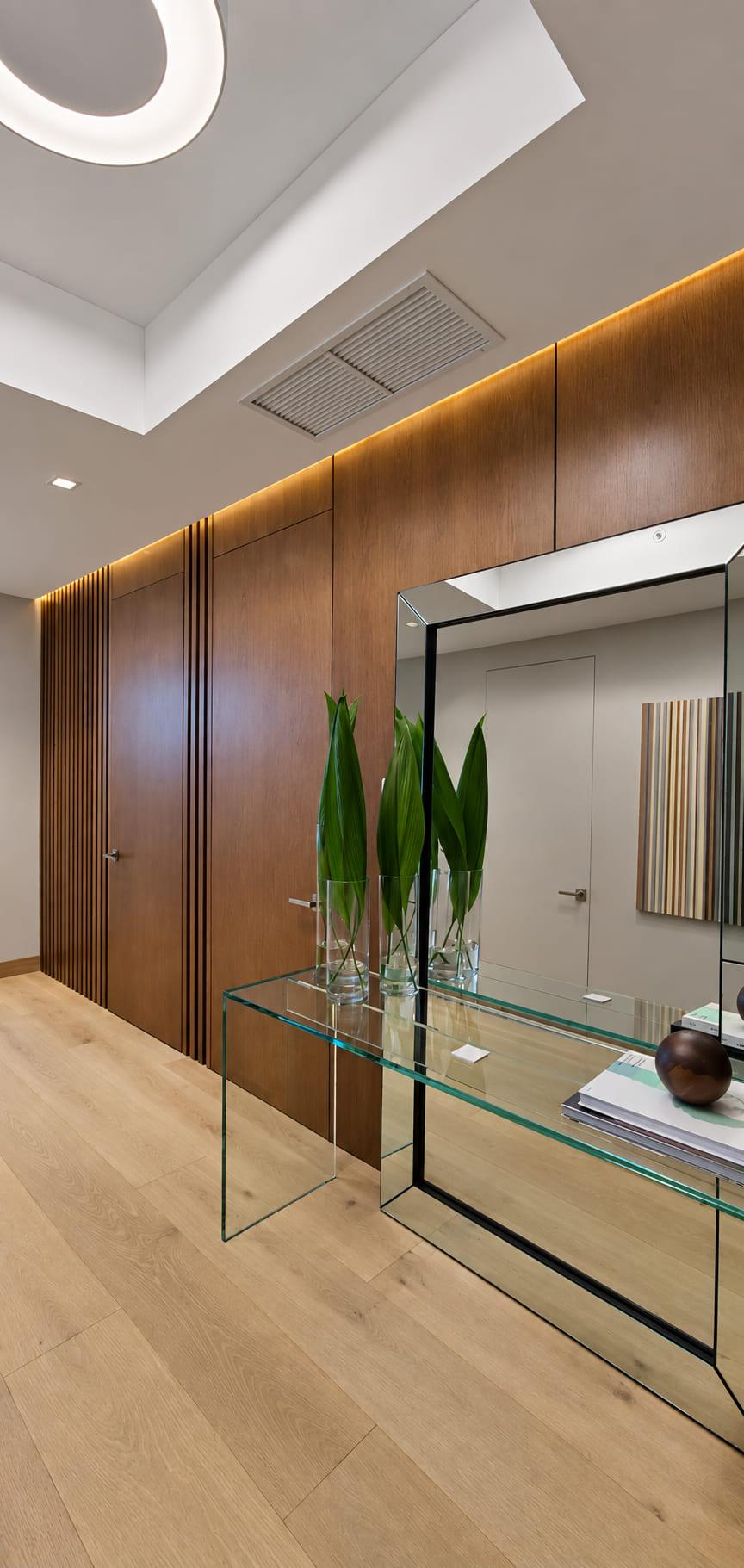 Glass console table and framed mirror against a walnut panelled entrance wall