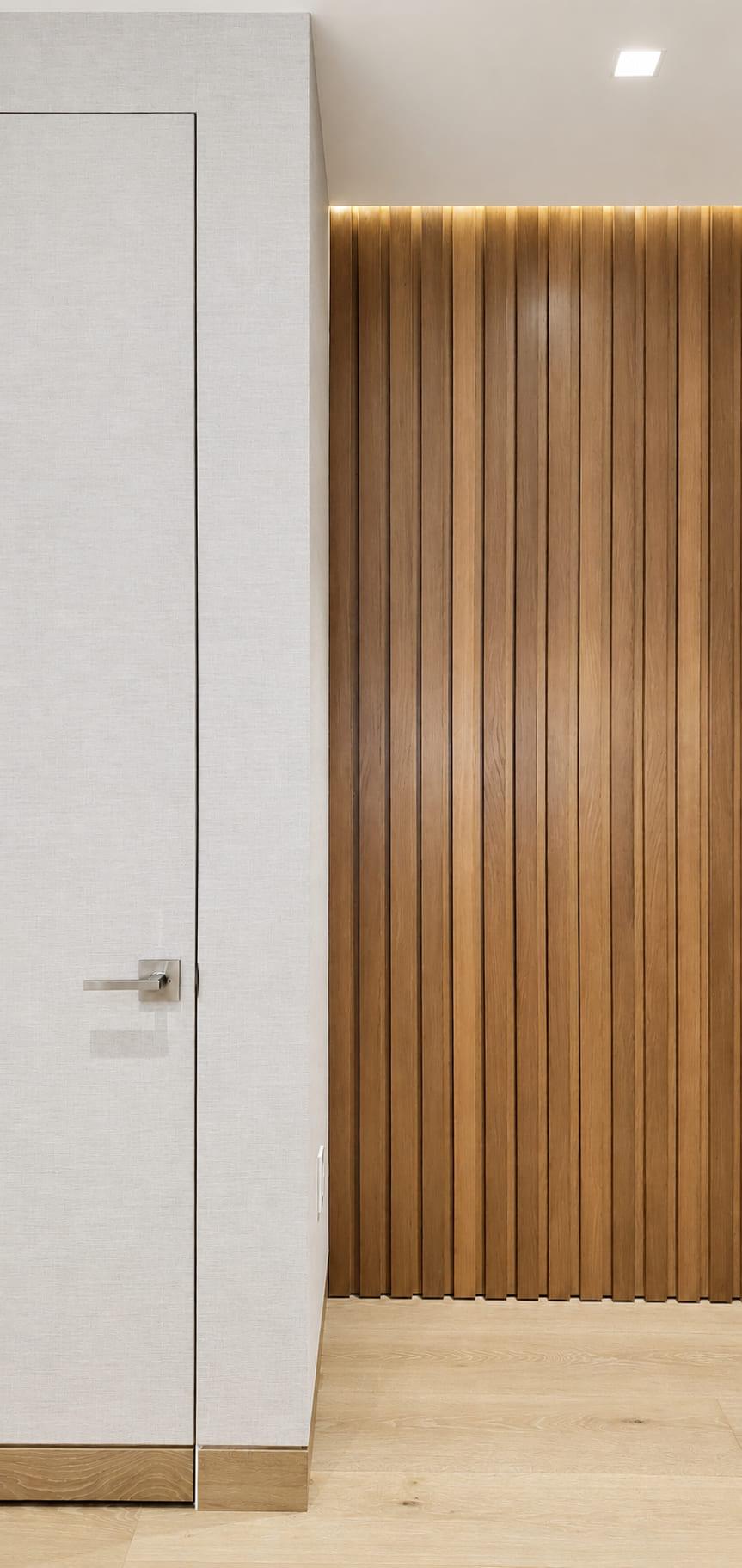 Flush linen-finish door with no architrave, next to a lit walnut slat wall