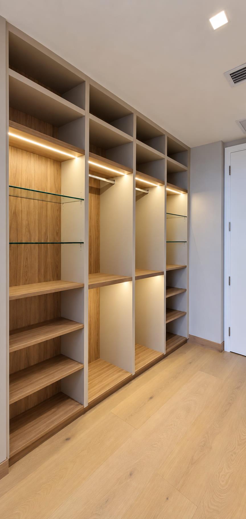 Oak dressing-room bay with glass shelves and a lit hanging rail