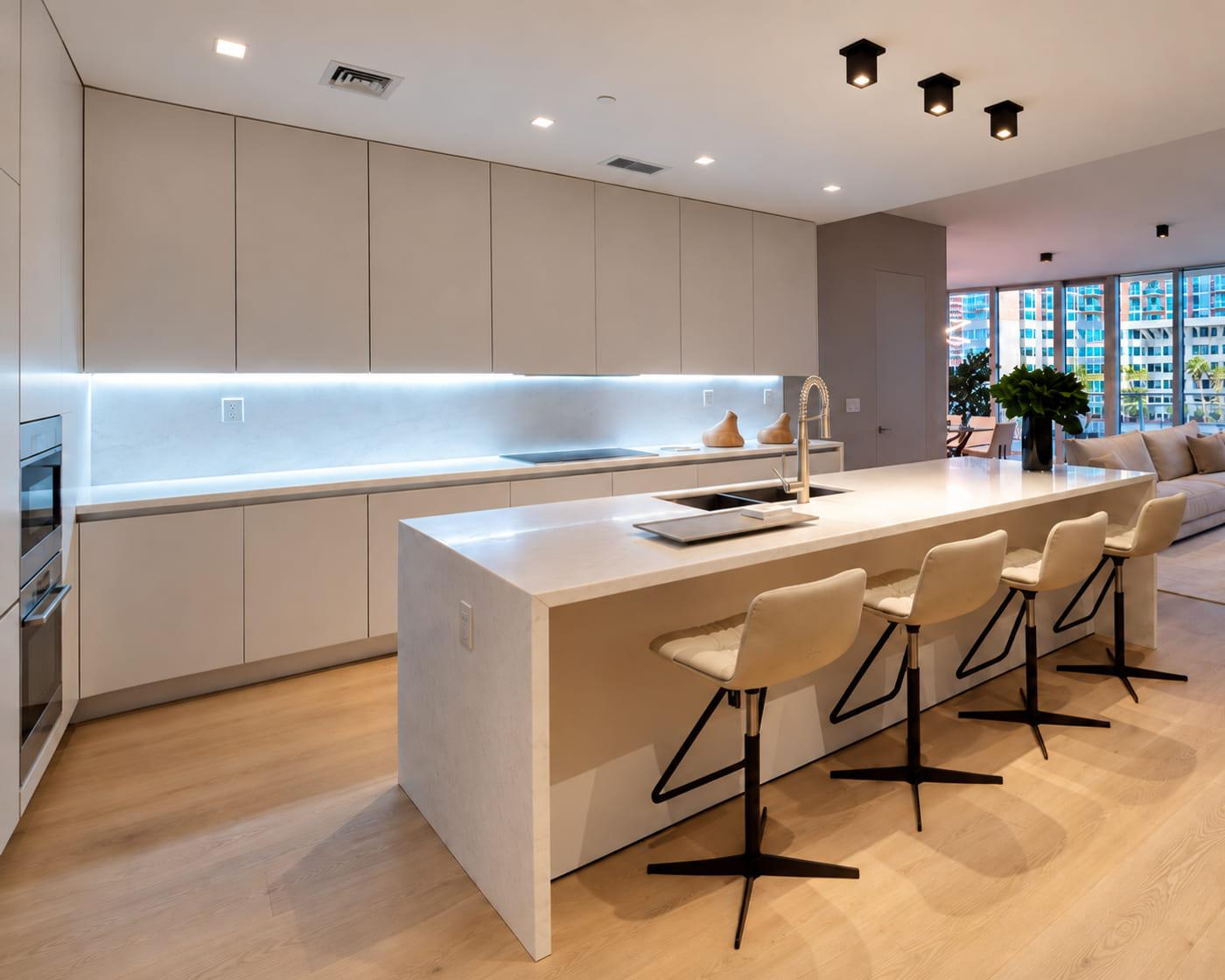 The finished kitchen in matt lacquer with a stone island and a lit splashback