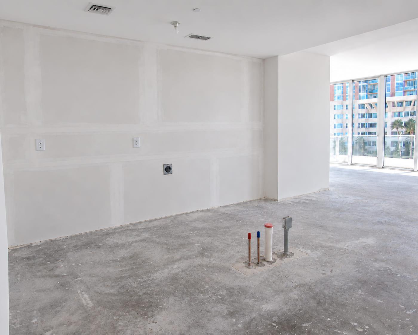 The kitchen wall as received: patched drywall, sockets and capped services on the slab