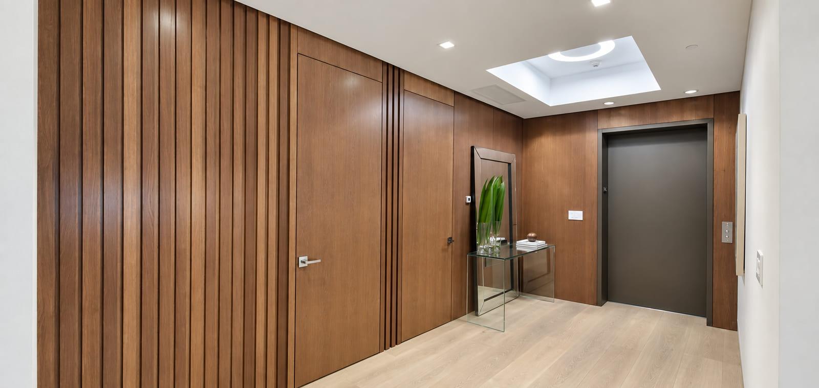 Private lift landing lined in walnut, with a lit oculus in the ceiling