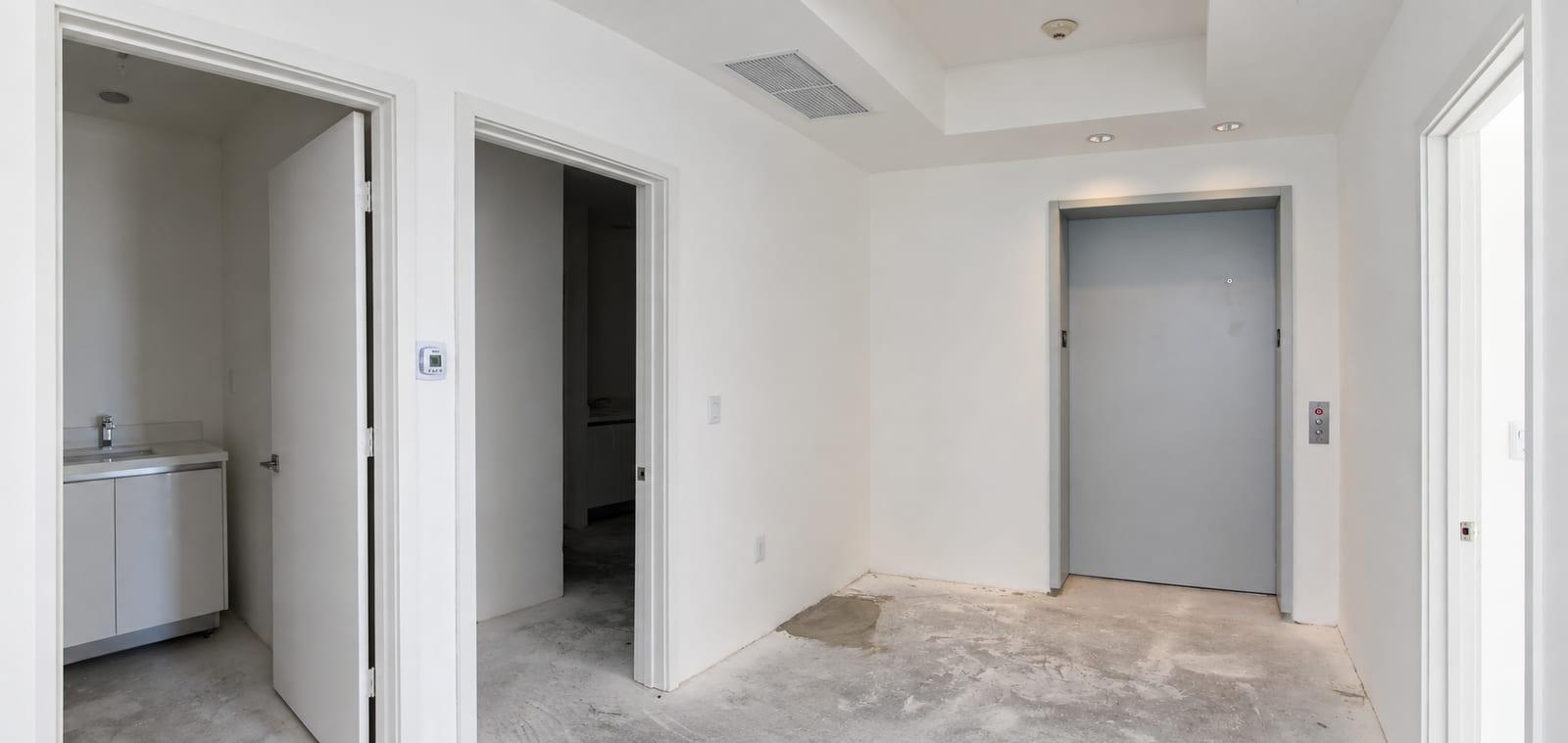 The lift landing as received: taped drywall, bare concrete and a grey lift door