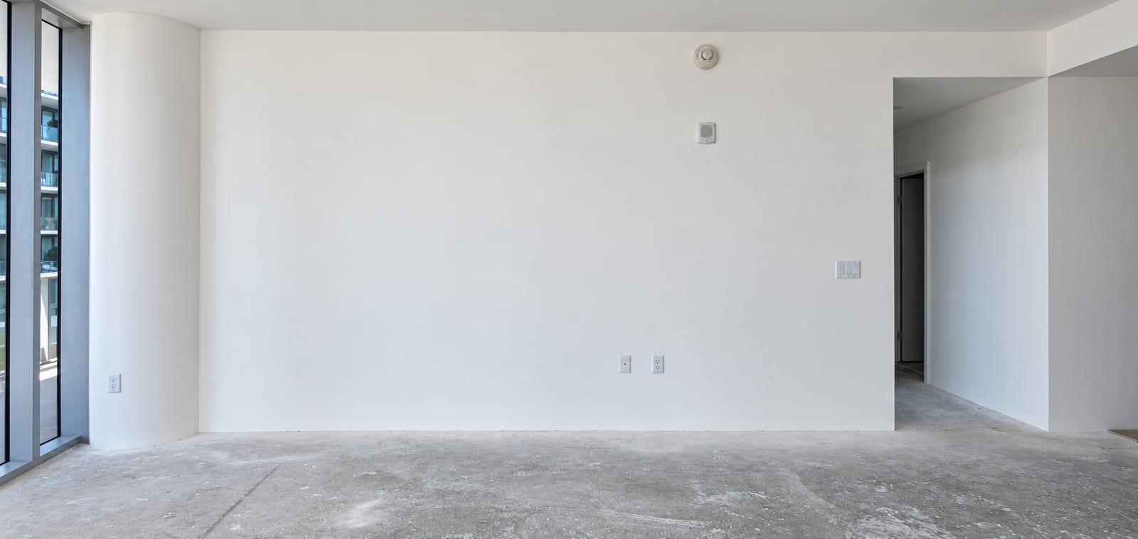 A blank drywall wall over a bare concrete floor, with the balcony to the left