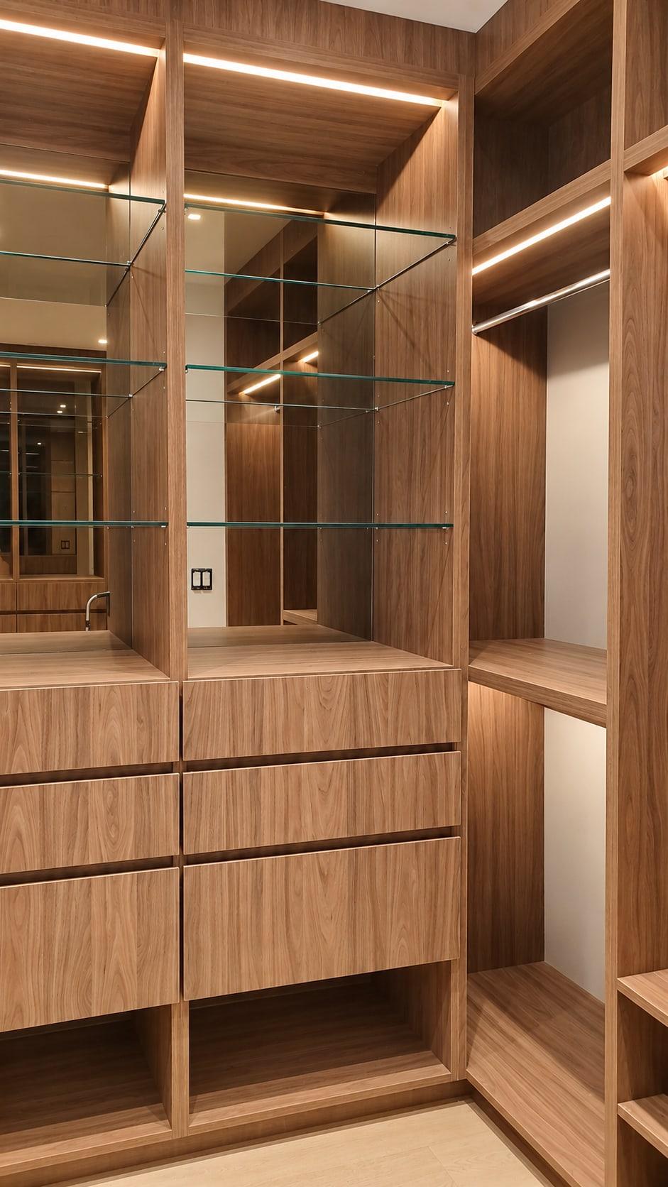 Walnut wardrobe with two bays of drawers under glass shelves and lit hanging rails at either end, a strip of light under every shelf