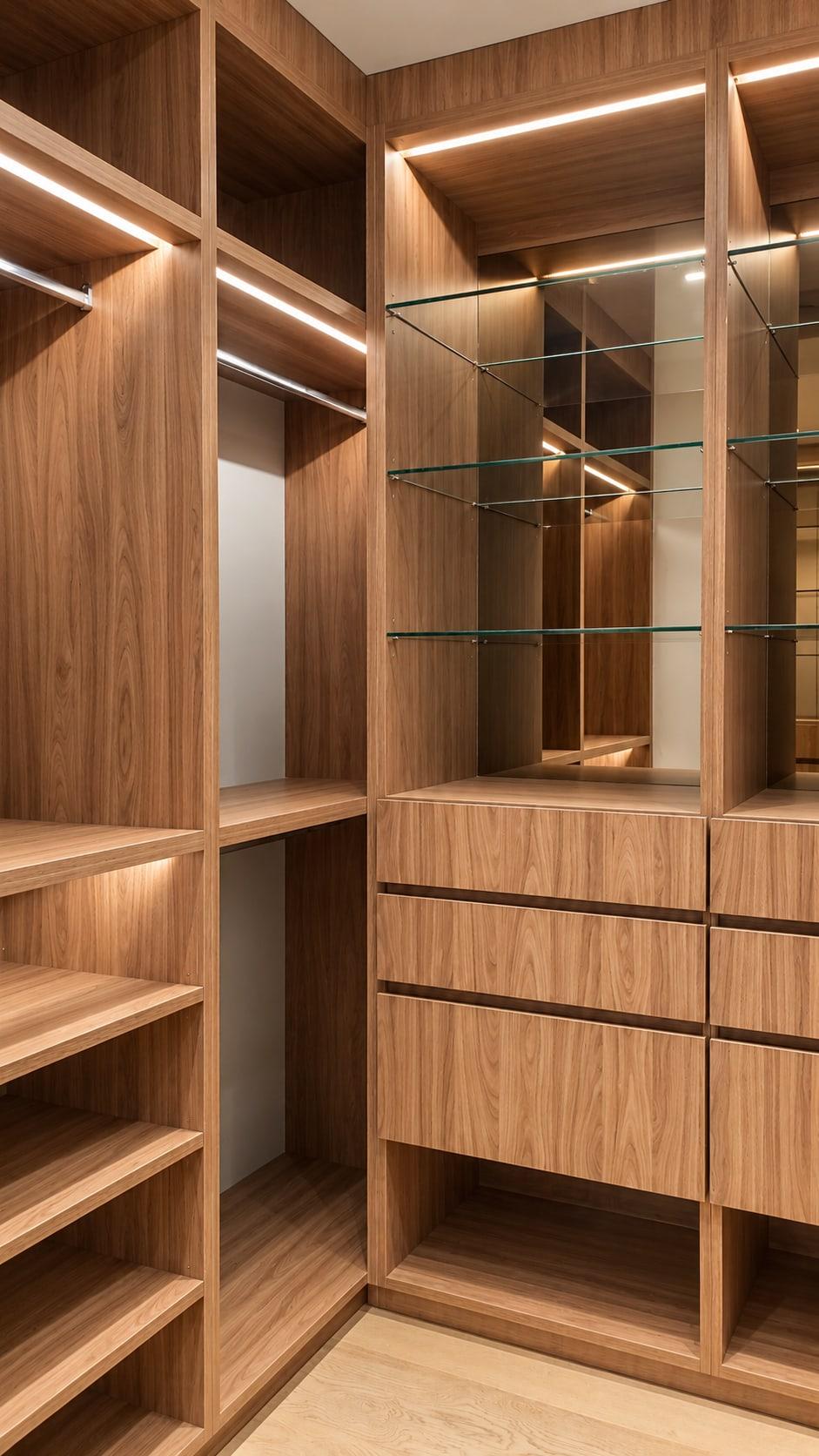 Corner of the walnut wardrobe: open shoe shelves and a lit rail on one side, drawers under glass shelves on the other